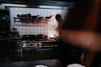 A cook in his kitchen with flames on the pan.