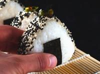 Un onigiri avec des graines de sésame tenu en main